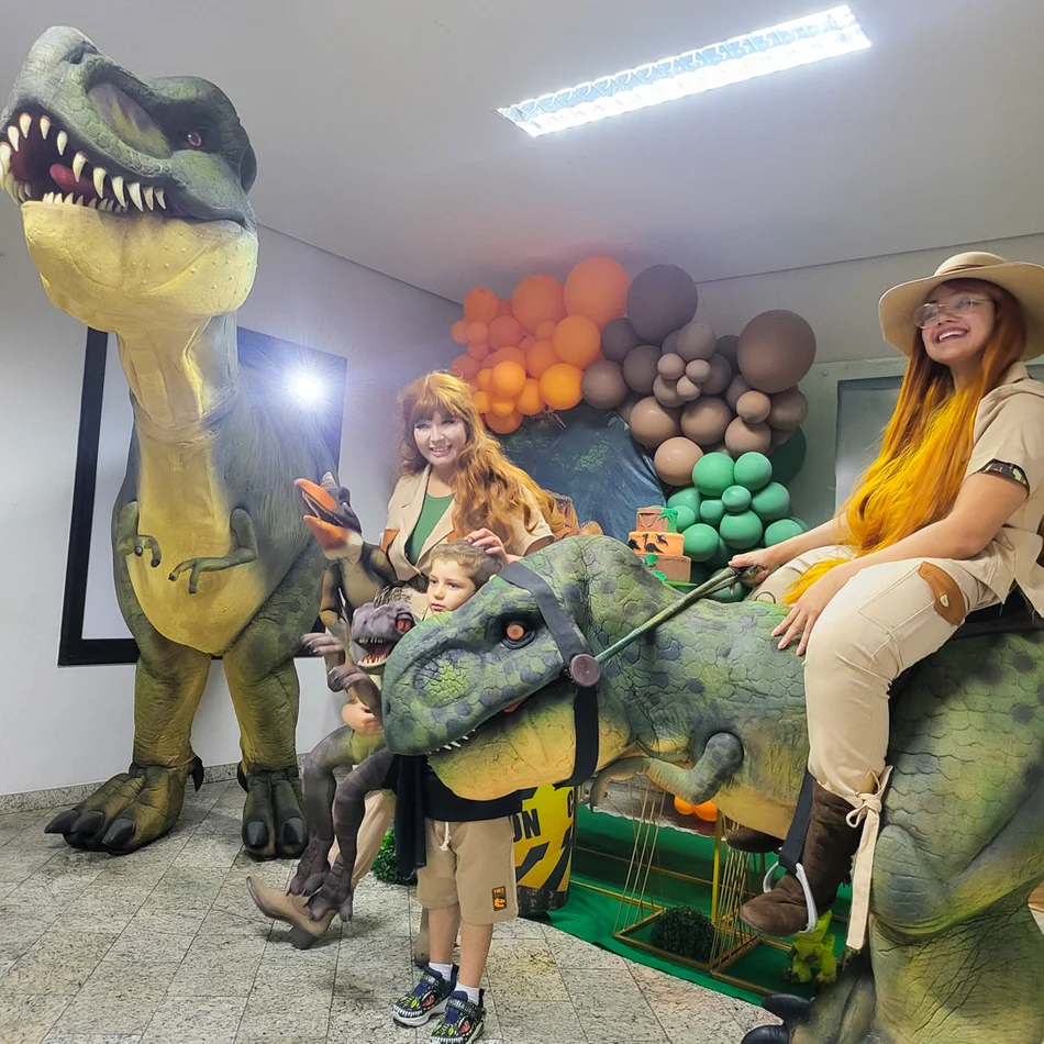 Criança pequena abraçando dinossauro baby com equipe de dinossauros personagens vivos em Alphaville